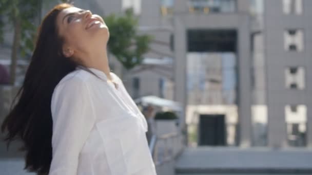 Donna d'affari bruna di successo in camicia bianca e con i capelli lunghi che soffiano guardando verso l'alto accanto al suo edificio per uffici — Video Stock