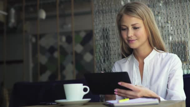A trabalhar no café. Jovem bela mulher de cabelo longo sentado à mesa e usando computador tablet interior . — Vídeo de Stock