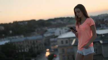 Çatı da akıllı telefon mesajları okuma esmer kadın hareketli görünümü, arka plan olarak gün batımında cityscape