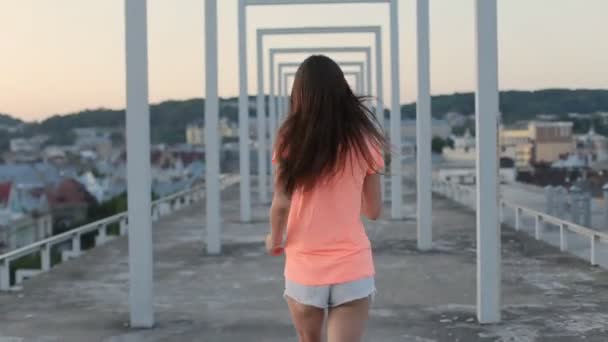 Mooie brunette meisje in oranje t-shirt en shorts loopt Terugkijkend door gebogen passage op het dak — Stockvideo