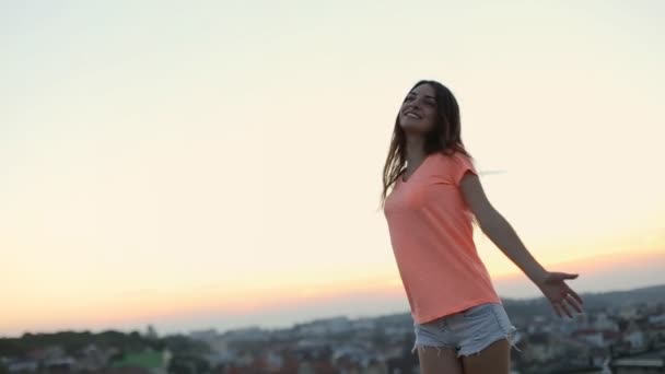 周囲の美しい景色を眺めながら屋根の上に立つ若い女性は、腕を上げて上下にジャンプします。 — ストック動画