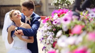 Yakışıklı damat yavaşça peçe gelini arkadan kucaklayan, el ele tutuşarak ve Bahçe çiçekli arch yakınındaki gülümseyen Mavi takım elbise