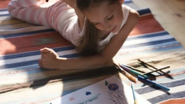 Досить маленька дівчинка малює кольоровими олівцями на підлозі в її кімнаті для розплідників — стокове відео