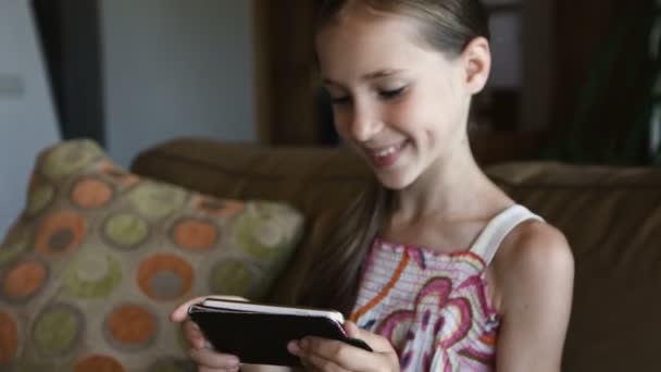 Schattig lachende klein meisje met behulp van moderne smartphone in woonkamer, close-up — Stockvideo