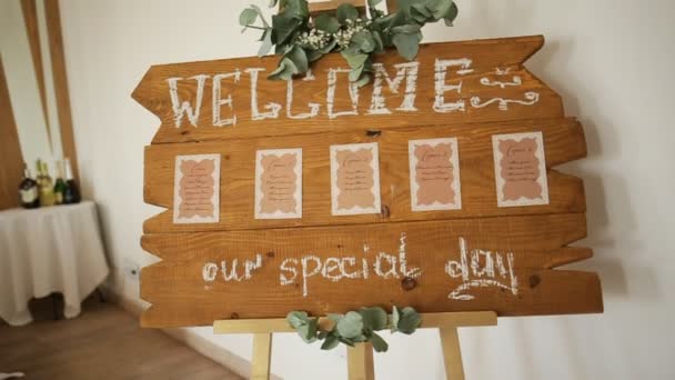 Plateau en bois fait à la main avec panneau de bienvenue dessus décoré d'eucalyptus sur pied blanc avec restaurant sur fond — Video