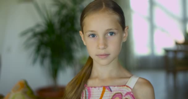 Retrato de una niña emocional positiva con el pelo largo y saludable y una dulce sonrisa posando a la cámara en el interior moderno — Vídeo de stock