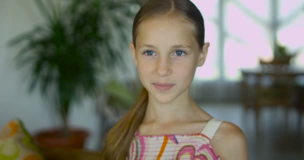 Retrato de una niña emocional positiva con el pelo largo y saludable y una dulce sonrisa posando a la cámara en el interior moderno — Vídeo de stock