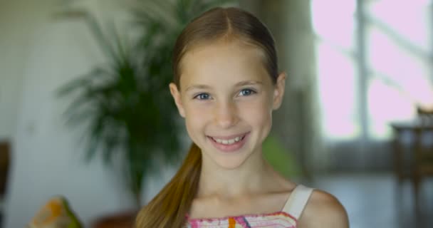 Retrato de una niña emocional positiva con el pelo largo y saludable y una dulce sonrisa posando a la cámara en el interior moderno — Vídeo de stock