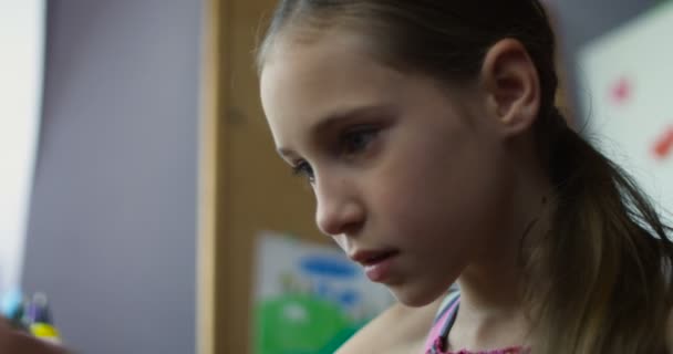 Pequeña colegiala sonriente sentada con teléfono inteligente jugando juegos en el escritorio en la guardería — Vídeos de Stock