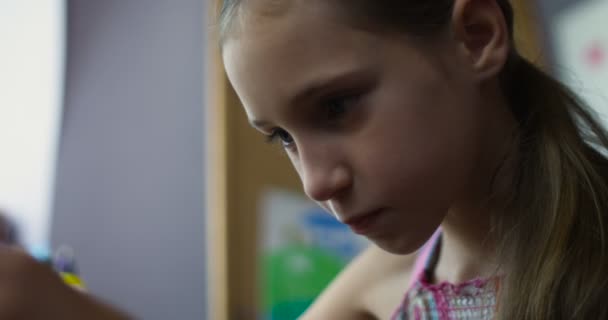 Pequeña colegiala sonriente sentada con teléfono inteligente jugando juegos en el escritorio en la guardería — Vídeos de Stock