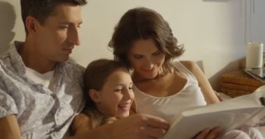 Beyaz aile yatak, anne, baba ve kızı okuma dergi döşeme gülümseyen mutlu