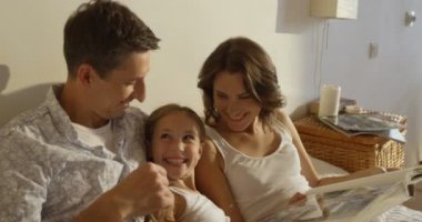 Anne, baba ve kızı birlikte yatakta döşeme bir kitap okuma pijama giymiş