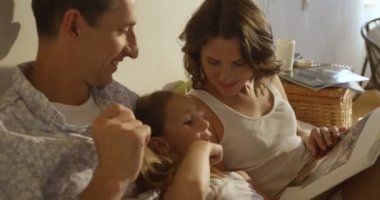 Anne, baba ve kızı birlikte yatakta döşeme bir kitap okuma pijama giymiş