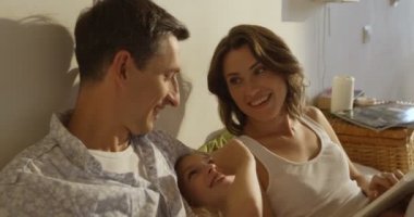 Anne, baba ve kızı birlikte yatakta döşeme bir kitap okuma pijama giymiş