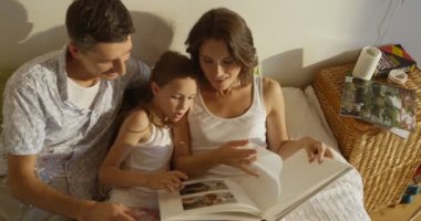 Anne, baba ve kızı birlikte yatakta döşeme bir kitap okuma pijama giymiş