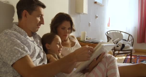 Feliz sonriente familia caucásica acostada en la cama, madre, padre e hija leyendo la revista — Vídeos de Stock