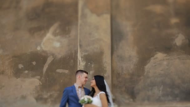 Pretty bride and handsome groom kissing on the street, near brown wall — Stock Video