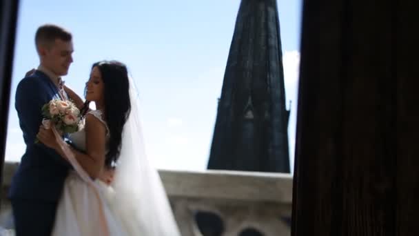 Hermosa novia y novio tomados de la mano abrazando cara a cara en el antiguo balcón, paisaje urbano de fondo — Vídeos de Stock