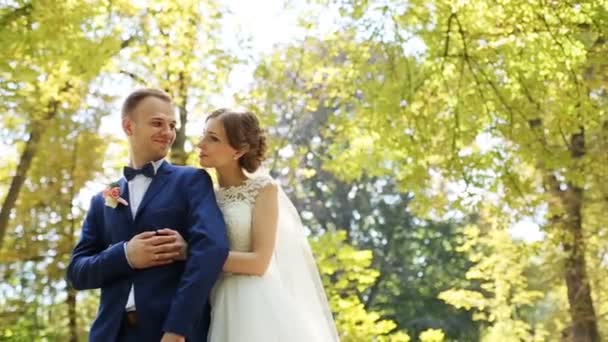 Bella sposa che abbraccia da dietro il suo bellissimo sposo nel parco autunnale sullo sfondo — Video Stock