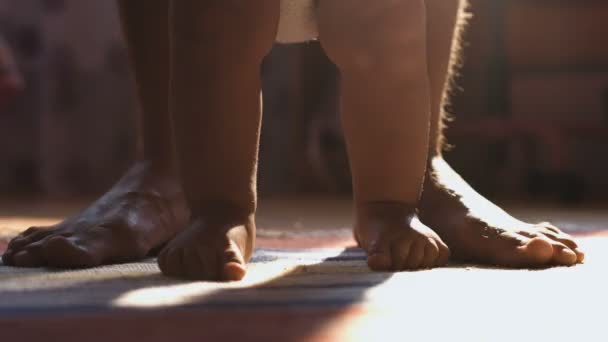 Primer plano del niño caminando sus primeros pasos con papá detrás, en la habitación soleada — Vídeo de stock