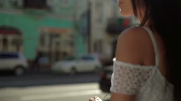 Uma jovem morena feliz menina em roupas casuais elegantes usando óculos de sol andando pela rua em uma bela cidade no dia ensolarado — Vídeo de Stock