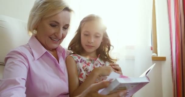 Young girl and grandmother watching together photo album, sitting in cozy interior — Stock Video