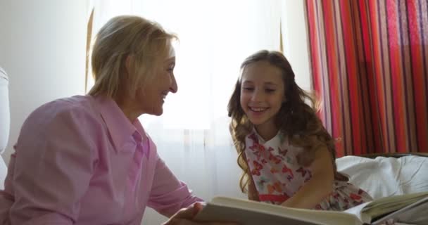 Granny sitting on couch next to her granddaughter and looking through photo album — Stock Video