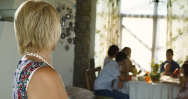 Encantadora mujer mayor posando en la cámara y la familia sentada en la mesa de comedor en segundo plano — Vídeos de Stock