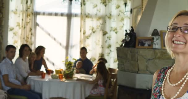 Encantadora mujer mayor posando en la cámara y la familia sentada en la mesa de comedor en segundo plano — Vídeos de Stock