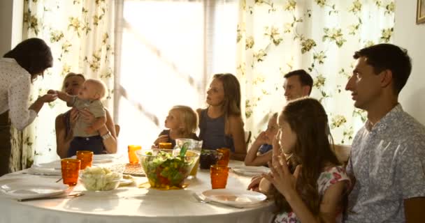 Ampliado grupo familiar sentado para refeição e olhando para a avó segurando seu neto — Vídeo de Stock