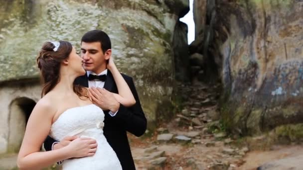 La novia y el novio se abrazan en la naturaleza. La pareja está de pie frente a las rocas — Vídeos de Stock