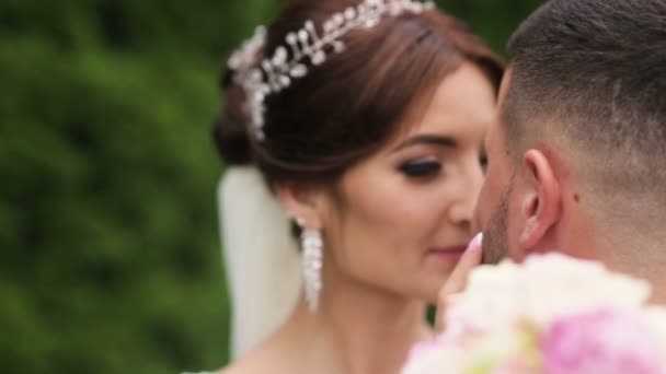 Feliz novia recién casada y novio besándose, dándose cuenta de que están casados ahora. Tiro al aire libre con parque de verano como fondo — Vídeo de stock