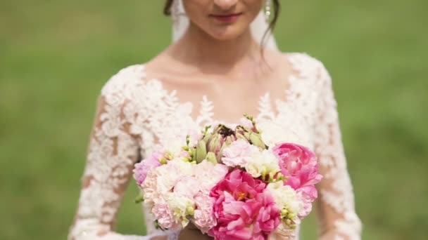 Porträt einer Braut im Brautkleid mit Blumen in einem sonnigen Park. — Stockvideo
