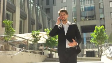 bir cep telefonu kullanarak çekici genç işadamı gülümseyerek. güzel, güneşli bir günde bir modern ofis önünde çekilen.