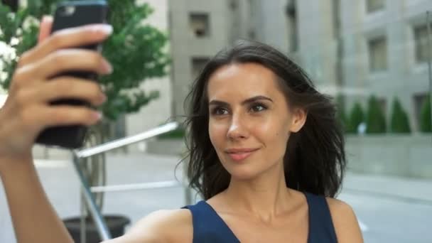 Mujer hermosa y sonriente tomar una foto de sí misma con un teléfono inteligente. selfie, tiro al aire libre, horizontal — Vídeos de Stock