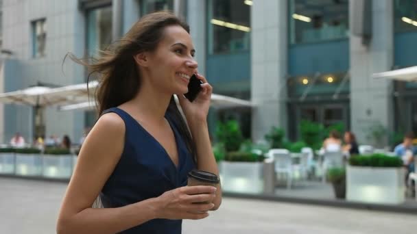 Atractiva joven morena empresaria llamando por teléfono móvil, caminando sosteniendo una taza de café . — Vídeos de Stock