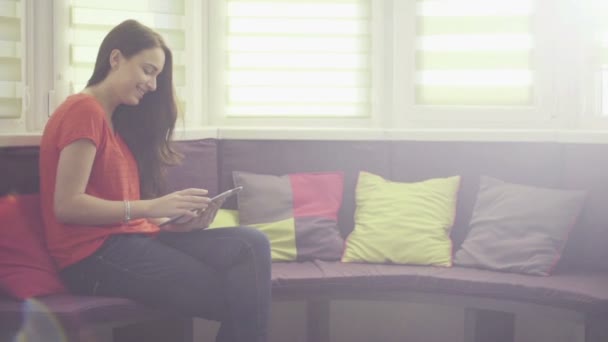 Розслаблена молода брюнетка сидить на дивані з планшетним ПК, вид збоку — стокове відео
