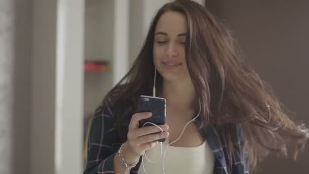 Musik- und Technologiekonzept - lächelndes Teenie-Mädchen in kariertem Hemd mit Kopfhörer, das zu Hause mp3 tanzen hört — Stockvideo