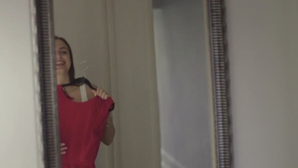 ミラーの彼女の反射を見て、自宅のワードローブでピンクのドレスにしようとしている若い魅力的な女性 — ストック動画