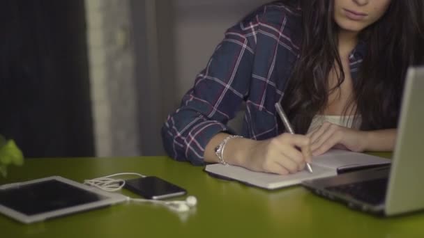 Jovem morena fazendo lição de casa e usando laptop sentado na mesa em casa — Vídeo de Stock