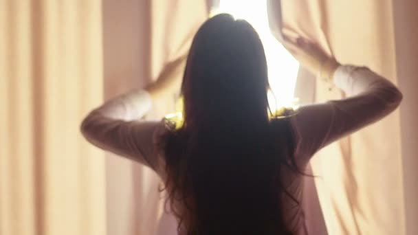 Bella ragazza apre tende su una grande finestra e lasciare che la luce nella stanza. Guardando fuori dalla finestra. Video al rallentatore — Video Stock