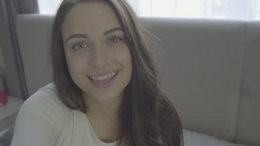Gülümseyen güzel esmer kanepede rahatlatıcı ve oturma odasında kamera bakarak
