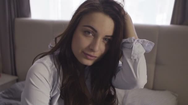 Porträtt av en vacker ung brunett kvinna leende på kameran sitter på soffan i vardagsrummet hemma — Stockvideo
