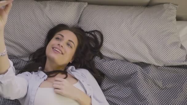 Красивая молодая женщина делает селфи с телефоном, лежащим на диване в гостиной — стоковое видео