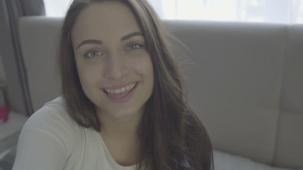 Glimlachend mooi brunette ontspannen op de Bank en kijken naar camera in de woonkamer — Stockvideo
