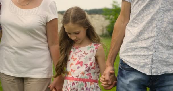 Ouders en gelukkige dochter wandelen in de zomertuin. Meisje speelt het houden van handen van ouders. — Stockvideo