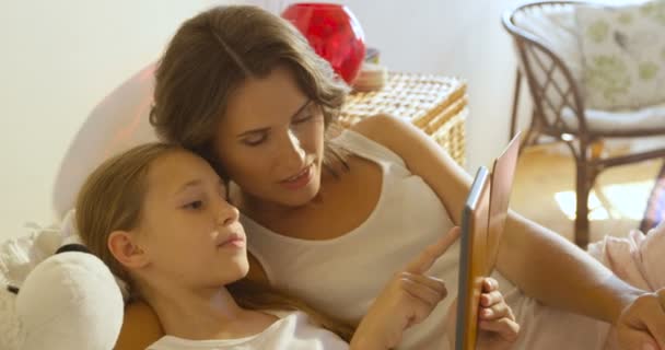 Primer plano de la madre y la hija acostadas en una cama en casa juntas, usando una tableta digital . — Vídeo de stock