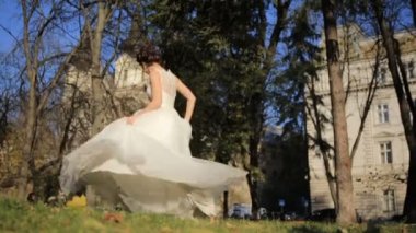 Genç güzel gelin parkta duruyor ve elbisesini yavaş çekimde sallıyor.