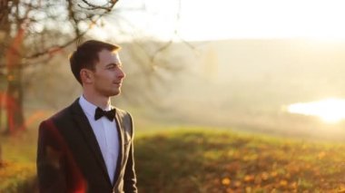 kahverengi bir yay ile bir takım elbise şık esmer gülümseyen damat yavaş hareket yakın çekim yürüyüş sonbahar parkı tutar