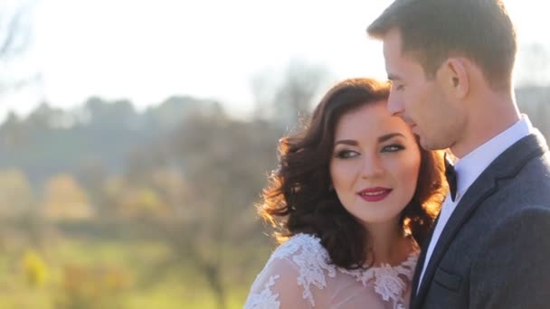 Splendida bionda giovane sposa e affascinante sposo in posa al tramonto girato al rallentatore da vicino — Video Stock